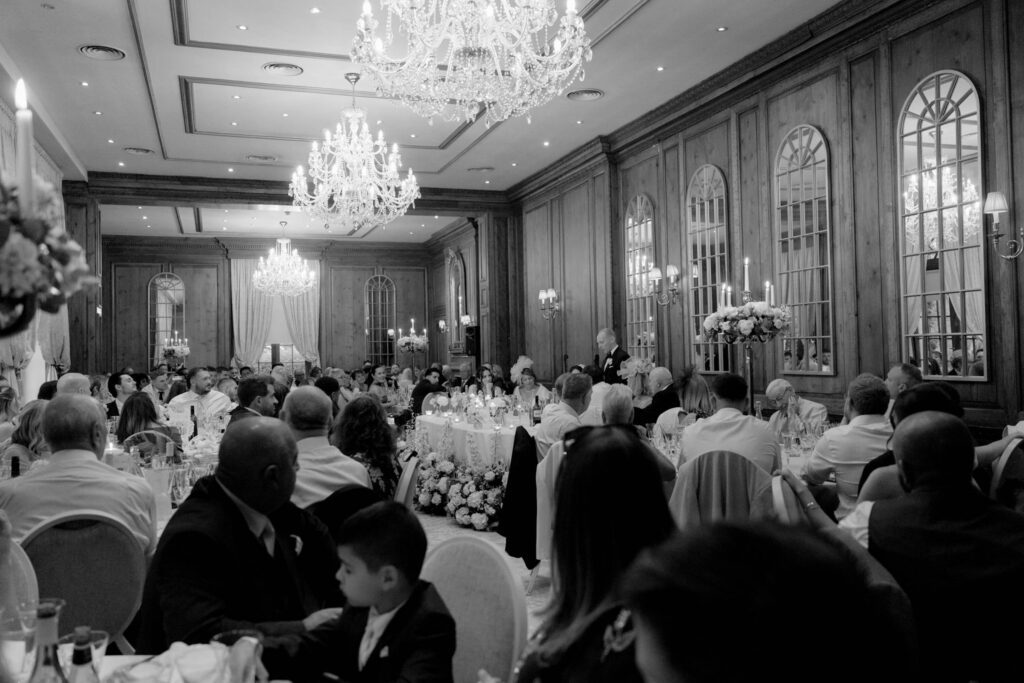 Wedding breakfast speech at Hedsor House, Buckinghamshire, captured in black and white by wedding photographer Emma Jane Lewis, with crystal chandeliers and candlelit reception room
